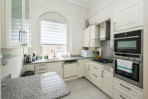 a kitchen with white cabinets and a large window at Four Beds by the Station in London