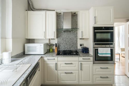 a white kitchen with white cabinets and appliances at Four Beds by the Station in London