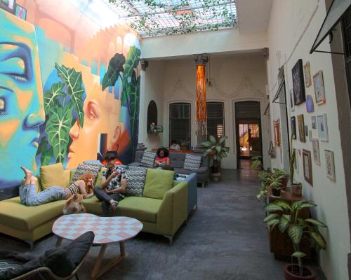 a living room with people sitting on couches and a mural at Art House Hostel Guadalajara in Guadalajara