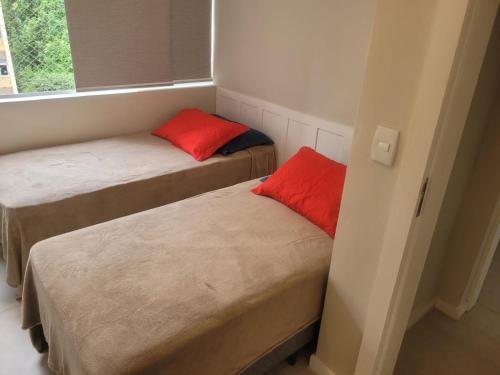 Duas camas com almofadas vermelhas num pequeno quarto em Apartamento em Ipanema no Rio de Janeiro