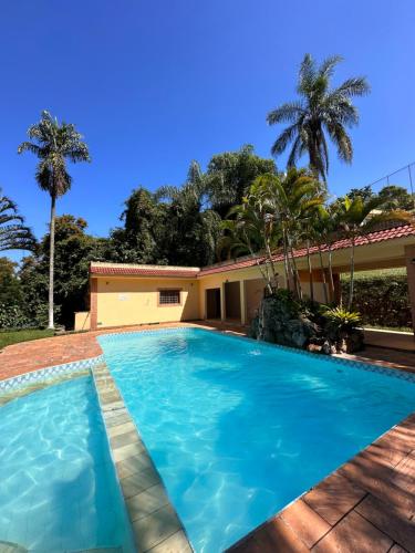 a swimming pool in front of a house with palm trees at Pousada Canto da Enseada in Nazaré Paulista