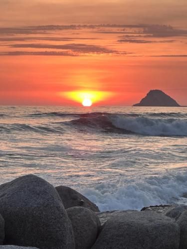 a sunset over the ocean with rocks on the beach at La isla surf Camp de punta hermosa in Punta Hermosa