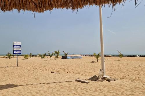 plaża ze słomianym parasolem i znakiem na niej w obiekcie Villa My Moon - en bord de mer au coeur de Saly w mieście Saly Portudal