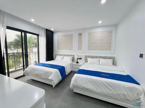 2 camas en una habitación blanca con ventana en Royal Beach Villa Sonasea Vân Đồn Quảng Ninh 