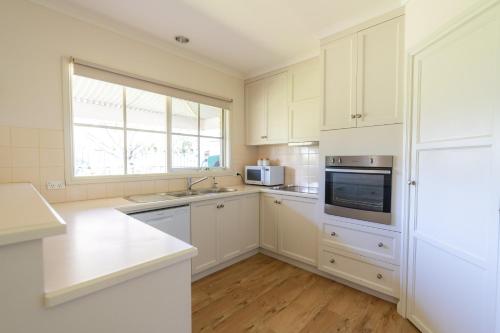 a kitchen with white cabinets and a sink and a microwave at The Royal Cottage in Mildura