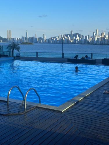 a large swimming pool with a city in the background at Loft em prédio frente mar in Balneário Camboriú