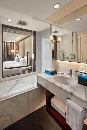 a bathroom with a tub and a sink and a bed at Mövenpick Hotel Hanoi Centre in Hanoi