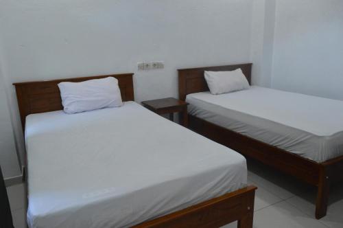 two beds with white sheets in a room at Mahoni Guest House Labuan Bajo in Labuan Bajo