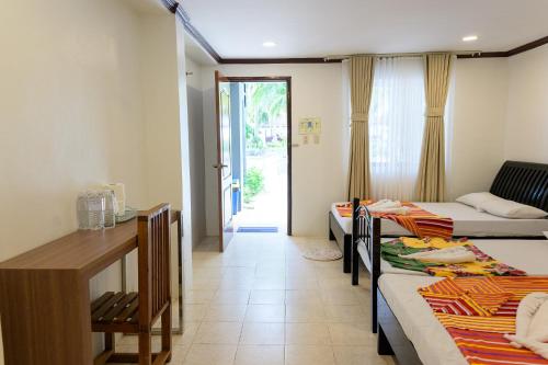 Habitación con 3 camas, mesa y escritorio. en D' Elmer's Resort and Convention Hotel, en Dinadiwan