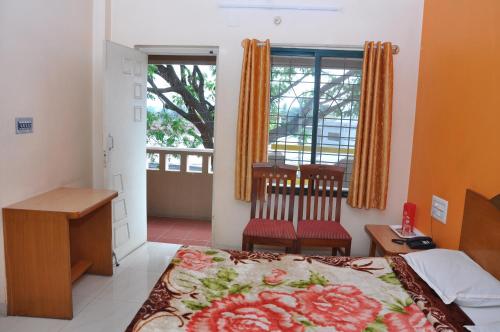 a bedroom with a bed and a desk and a window at Vinayaka Deluxe Lodge in Kushālnagar