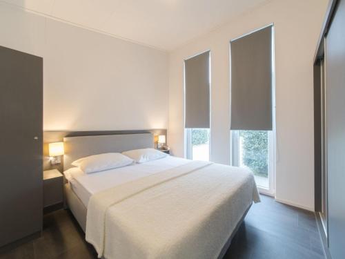 Un dormitorio con una gran cama blanca con dos ventanas. en Modern chalet at the edge of a forest, en Wemeldinge