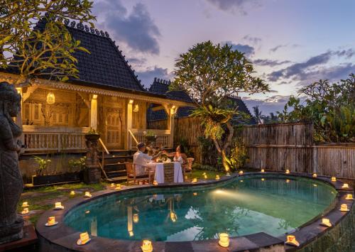 a group of people sitting around a table by a pool at Wooden Ganeca Villas by GenuineHost in Ubud