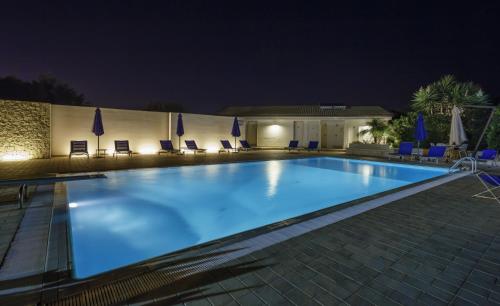 a swimming pool at night with chairs and umbrellas at Sikelika Residence Sul Mare in Scoglitti