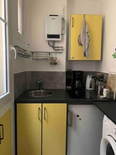 Elle comprend une petite cuisine avec des placards jaunes et un évier. dans l'établissement Appartement de charme à proximité des puces, à Saint-Ouen