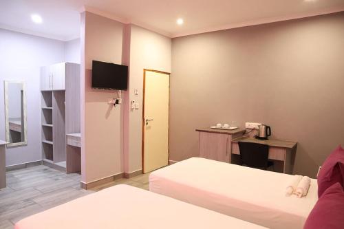a room with two beds and a desk with a television at Amariah Lodge in Kasane