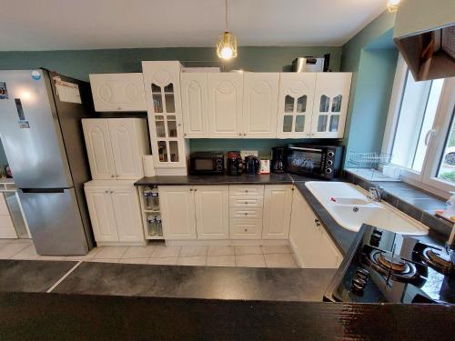 une cuisine avec des armoires blanches et un réfrigérateur en acier inoxydable dans l'établissement Maison spacieuse avec jardin proche Disney, à Tancrou
