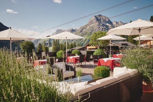 a restaurant with tables and umbrellas with mountains in the background at Burg Hotel Oberlech in Lech am Arlberg
