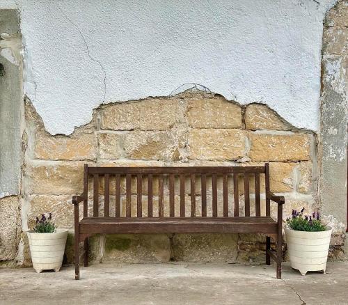 a wooden bench next to a stone wall with two flower pots at Rakousy22 in Rakousy
