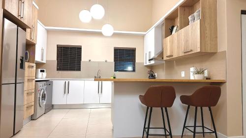 una cocina con armarios blancos y 2 taburetes en Upmarket apartment in the heart of Windhoek, en Windhoek
