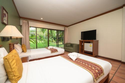 a hotel room with two beds and a television at Comsaed River Kwai Resort SHA in Kanchanaburi City