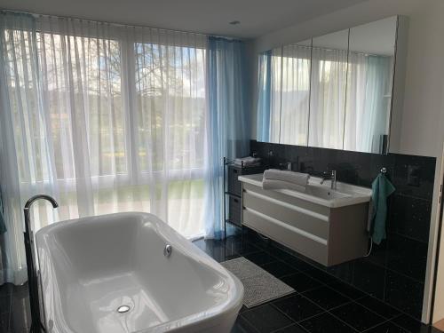 een badkamer met een bad, een wastafel en een spiegel bij Deluxe Doppelzimmer mit Pool und Aussicht in Dänikon