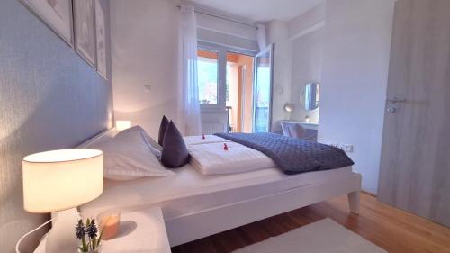 a white bedroom with a bed and a window at Apartman Lucille in Osijek