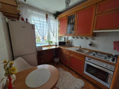 a kitchen with red cabinets and a table and a refrigerator at Przytulny apartament blisko MOLO GIŻYCKO in Giżycko
