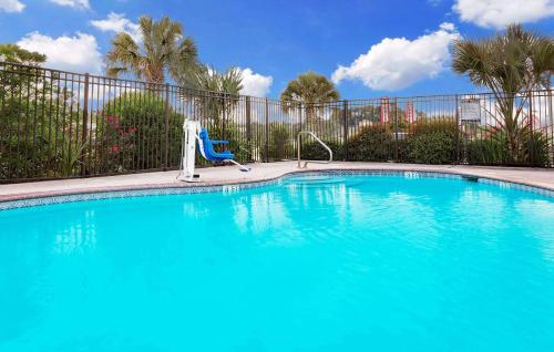 a blue swimming pool with a chair in front of a fence at Days Inn & Suites by Wyndham Opelousas in Opelousas