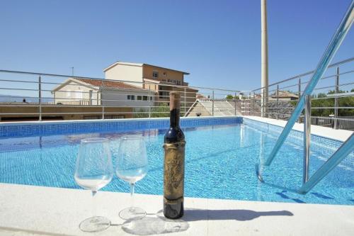 eine Flasche Wein und zwei Weingläser neben einem Pool in der Unterkunft Apartments Babaja in Omiš