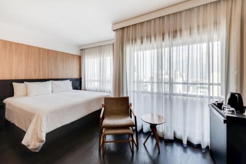 a hotel room with a bed and a chair and a window at Radisson São Paulo Paulista in Sao Paulo
