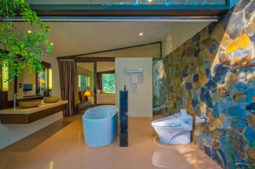baño con aseo y pared de piedra en Villa R331 Forest Flamingo Dai Lai Resort, en Phúc Yên