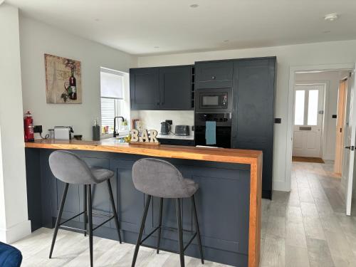 a kitchen with black cabinets and two bar stools at Brand New Big House with garden and free parking in Brentford