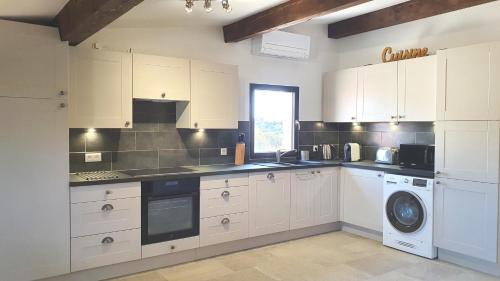 cocina con armarios blancos, lavadora y secadora en 'Au Coeur des Vignes' - private apartment & garden en Magalas