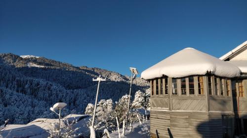 un edificio cubierto de nieve con una montaña en el fondo en Black Bear Cottage khajjiar, en Khajjiar 