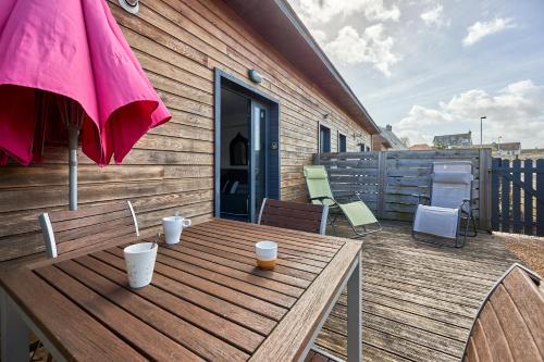 a wooden table with cups and an umbrella on a deck at Ethoucky - Maison à 300m de la plage in Bernières-sur-Mer