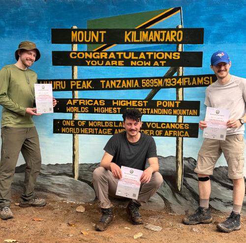 three men holding up certificates in front of a sign at Karibu Africa Home in Moshi