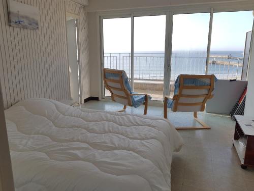 - une chambre avec un lit et deux chaises et un balcon dans l'établissement Appartement face mer 1 etoile - WIFI - Le Remblai, à Les Sables-dʼOlonne