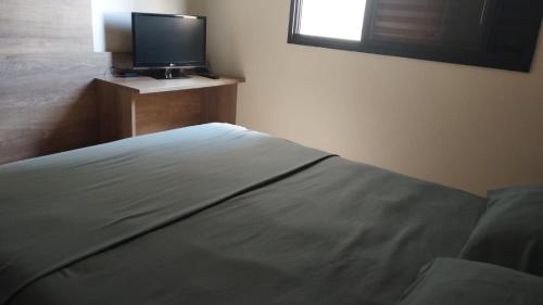 a bedroom with a bed and a flat screen tv at Quarto Bem no Centro Dourados in Dourados