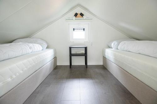 two white beds in a attic with a window at Camping de Konijnenberg Tiny House in Harderwijk