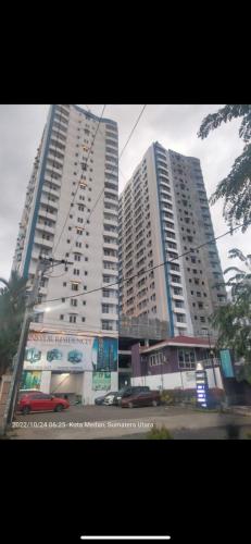 two tall buildings in a city with cars in front at Mansyur Residence Apartment Medan in Sunggal