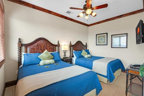 2 Betten in einem Schlafzimmer mit blauer Bettwäsche und einem Deckenventilator in der Unterkunft Arc de Texas -Louis XIV Suite in Johnson City