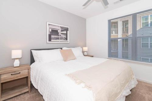 a white bedroom with a bed and a nightstand and two windows at Landing at San Marco Promenade - 1 Bedroom in San Marco in Jacksonville