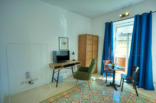 a living room with a desk and a television and blue curtains at Cozy 1bedroom, roof terrace near Valletta DAZZ1-2 in Il-Furjana
