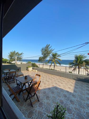 eine Terrasse mit Tischen und Stühlen und Strand in der Unterkunft Casa de Praia Suítes in Saquarema