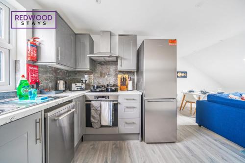 a kitchen with stainless steel appliances and a blue couch at BRAND NEW, 1 Bed 1 Bath, Modern Town Center Apartment, FREE WiFi & Netflix By REDWOOD STAYS in Aldershot