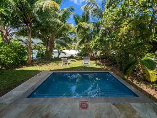 a pool in a yard with two chairs and palm trees at Maison La Plage by Simply-Seychelles in Eden Island