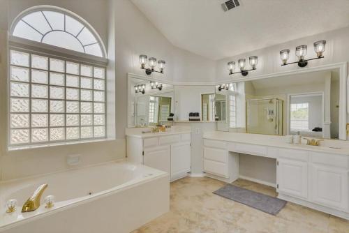 La salle de bains blanche est pourvue d'une baignoire et d'une grande fenêtre. dans l'établissement Amazing Modern Spacious Home with Pool, à Rowlett