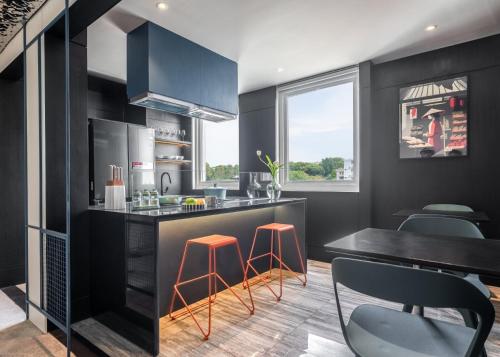 a kitchen with black cabinets and orange stools at M Village Nguyễn Kiệm - Cosmo Airport Hotel in Ho Chi Minh City