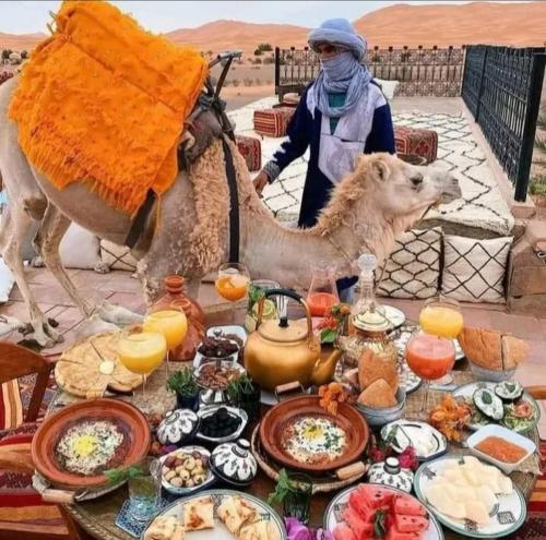 a camel and a woman standing next to a table of food at Desert Berber Camp in Merzouga