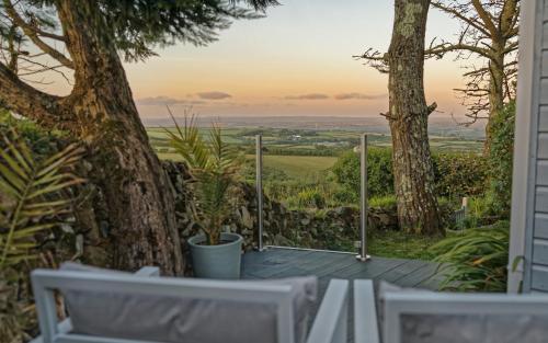 a porch with two white chairs and a tree at Scandi Cabin On A Hill, With Stunning Views Across Cornwall in Nancledra